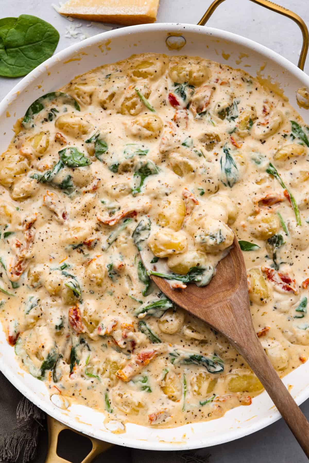 Creamy Tuscan Parmesan Gnocchi has the most incredible creamy sauce with spinach and sun-dried tomatoes. This is an easy comforting meal packed with flavor that can be on the dinner table in less than 30 minutes! Tuscan parmesan gnocchi in a white skillet.