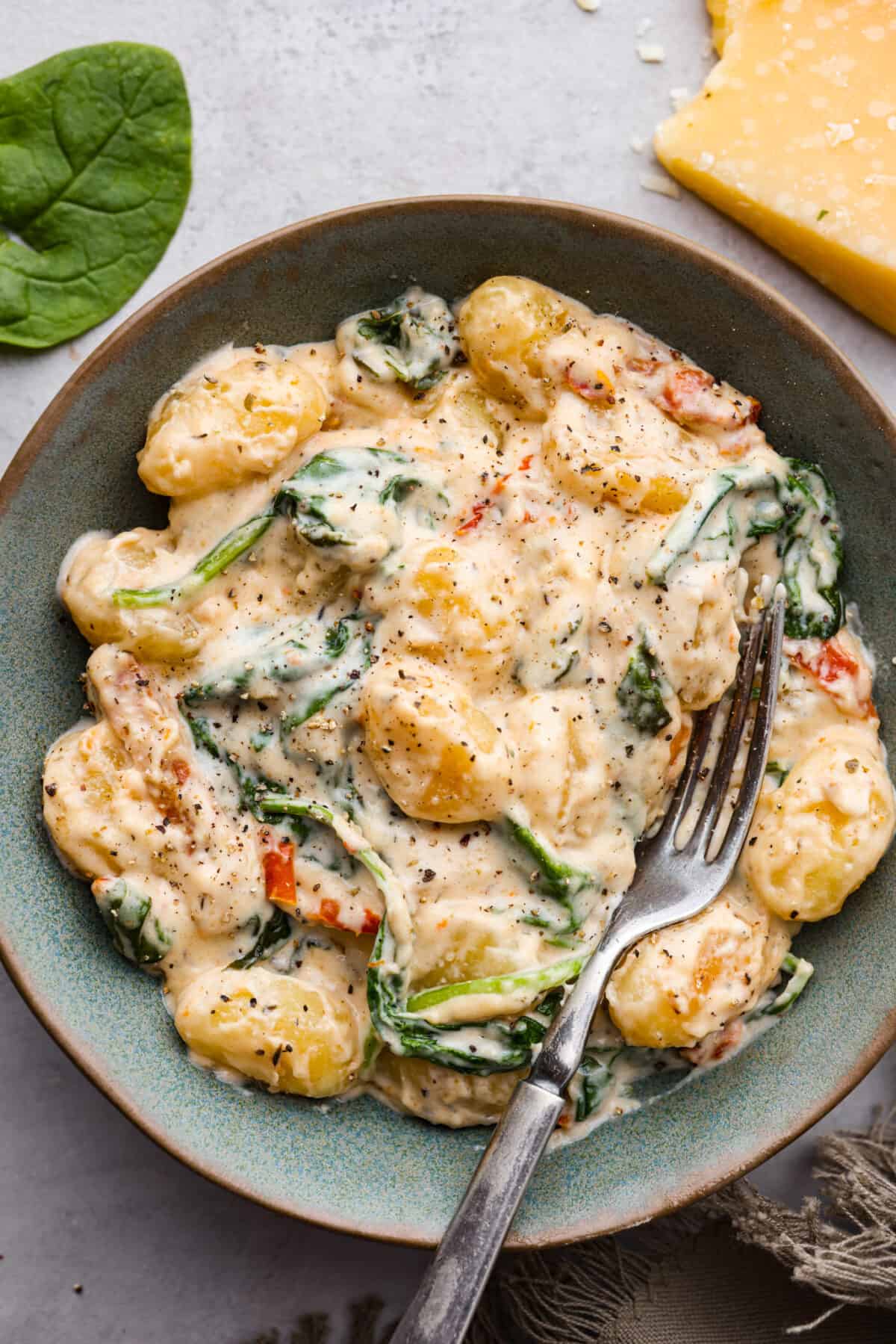 Creamy Tuscan Parmesan Gnocchi has the most incredible creamy sauce with spinach and sun-dried tomatoes. This is an easy comforting meal packed with flavor that can be on the dinner table in less than 30 minutes! A serving of Tuscan parmesan gnocchi in a gray bowl.