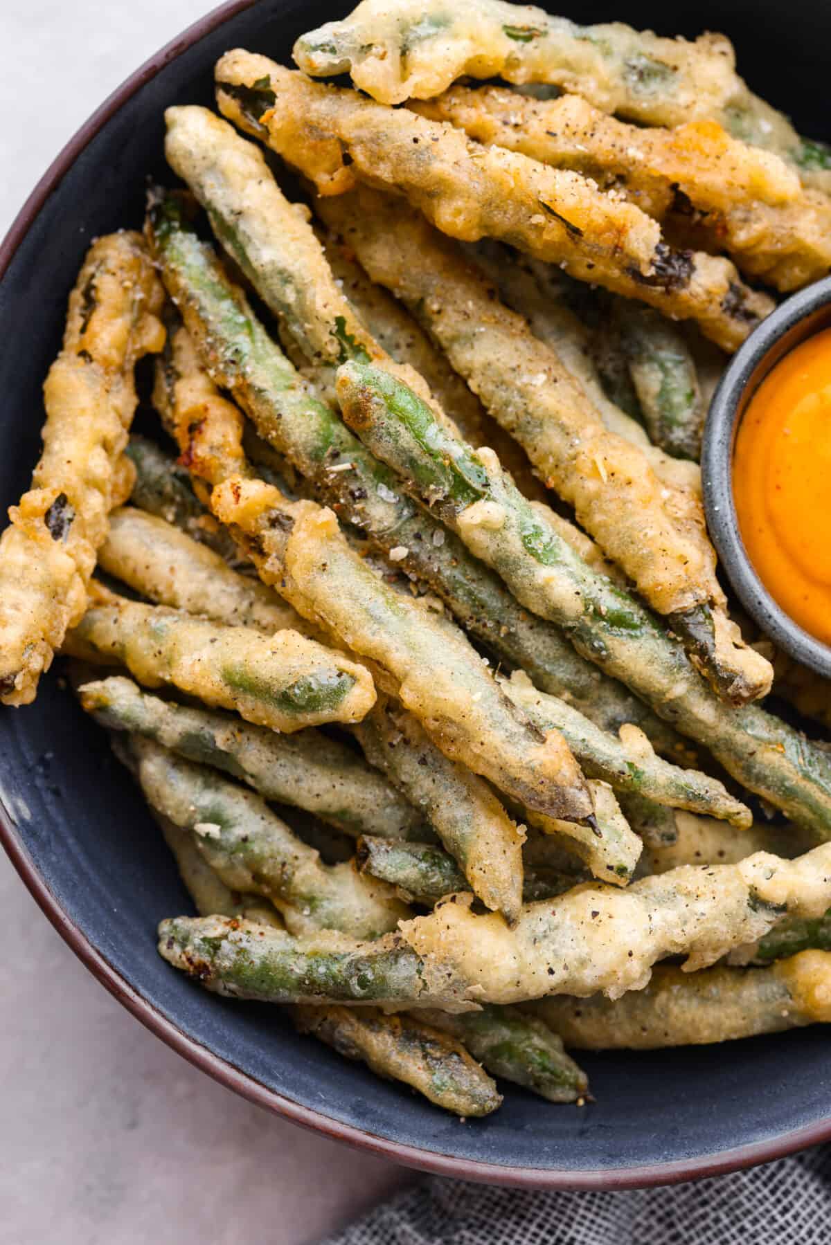 One of the best things on the menu at P.F. Changs is their Crispy Fried Green Beans. These green beans taste even better, and you can make them at home! They have a delightful crunch and are seasoned to perfection! A close up of the crispy friend green beans on a platter.