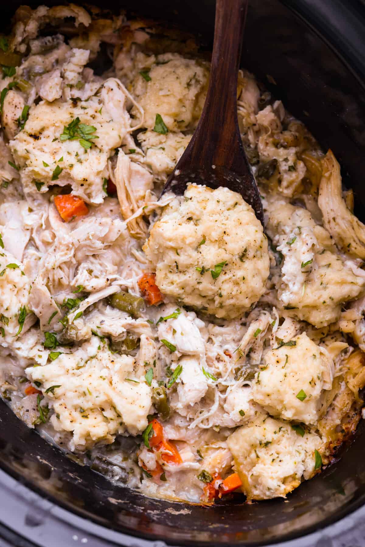 Crockpot chicken and dumplings...the ultimate comfort meal ready when you get home! Tender chicken and vegetables topped with homemade dumplings. Easy to assemble and slow-cooked to perfection. Top view of crockpot chicken and dumplings in a black crockpot.