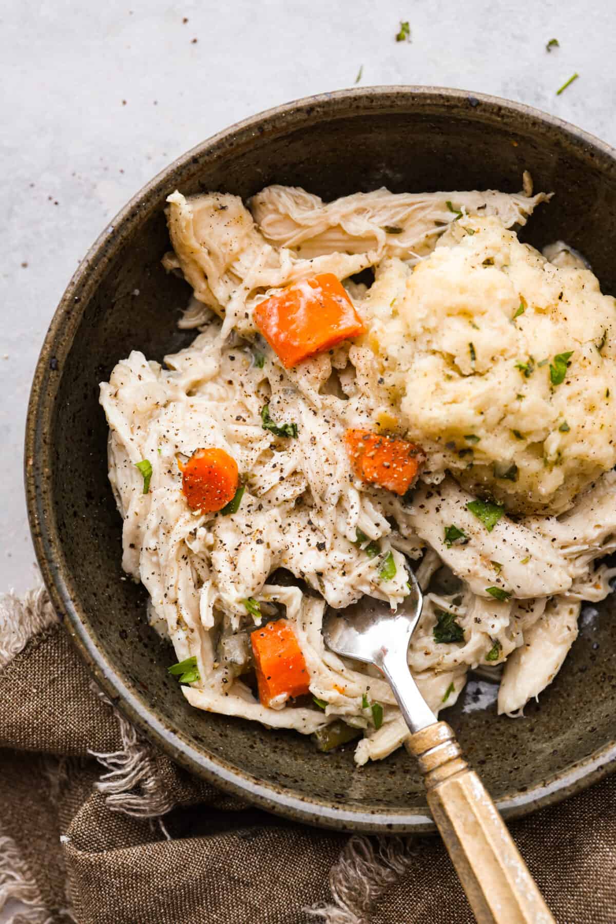 Crockpot chicken and dumplings...the ultimate comfort meal ready when you get home! Tender chicken and vegetables topped with homemade dumplings. Easy to assemble and slow-cooked to perfection. Chicken and dumplings in a brown bowl with a fork.