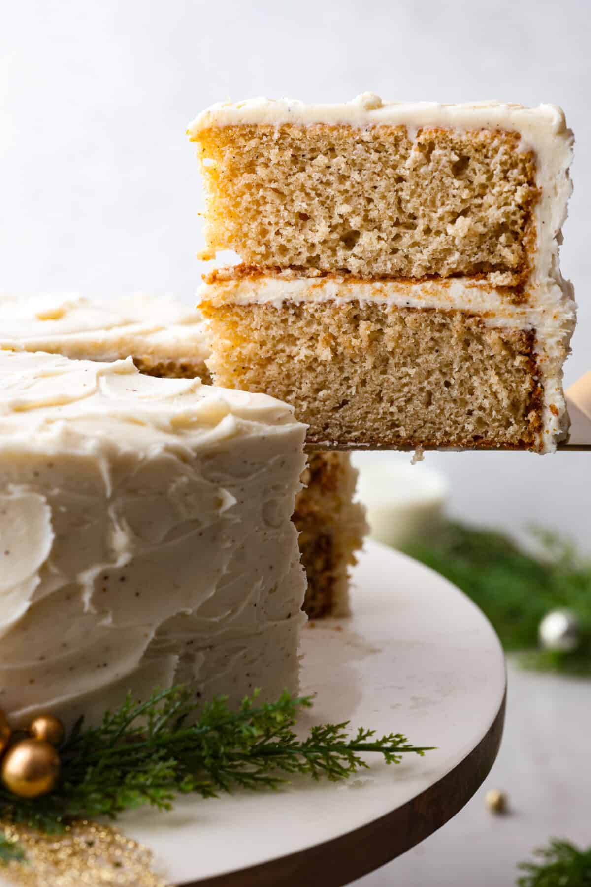 Festive eggnog cake is the perfect dessert to serve this holiday season! Make this moist eggnog-flavored cake bursting with delicious seasonal spices and layered with creamy eggnog buttercream! Close side view of a slice of cake lifting from the cake.