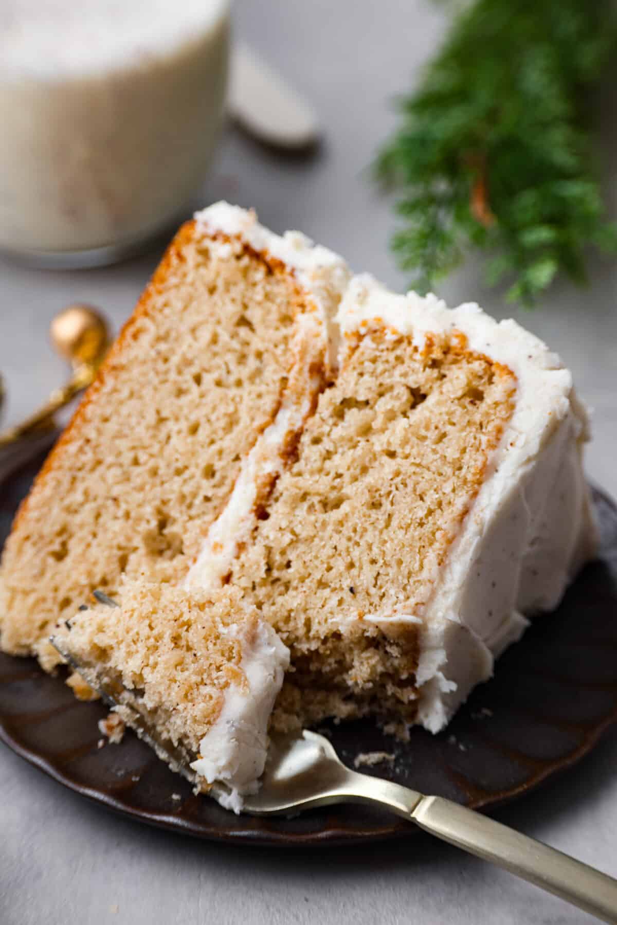 Festive eggnog cake is the perfect dessert to serve this holiday season! Make this moist eggnog-flavored cake bursting with delicious seasonal spices and layered with creamy eggnog buttercream! A slice of cake on a plate with a piece of cake on a fork.