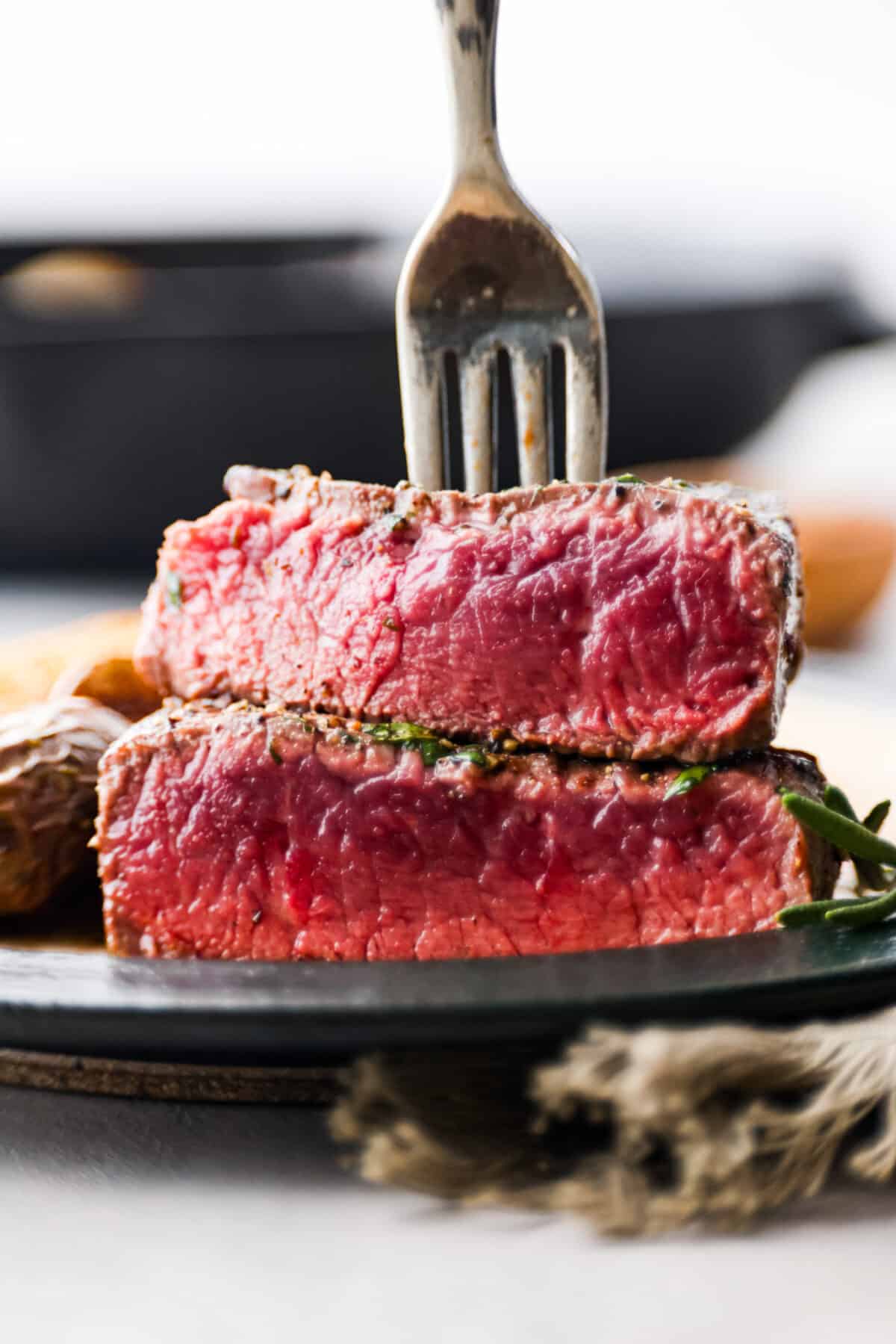 Juicy and succulent filet mignon is perfect for dinner or any special occasion! Tender steak is seasoned, seared, and basted with garlic herb butter. This is a steakhouse-quality recipe that is so easy to make at home! Close view of sliced filet mignon stacked on a plate with a fork in it.