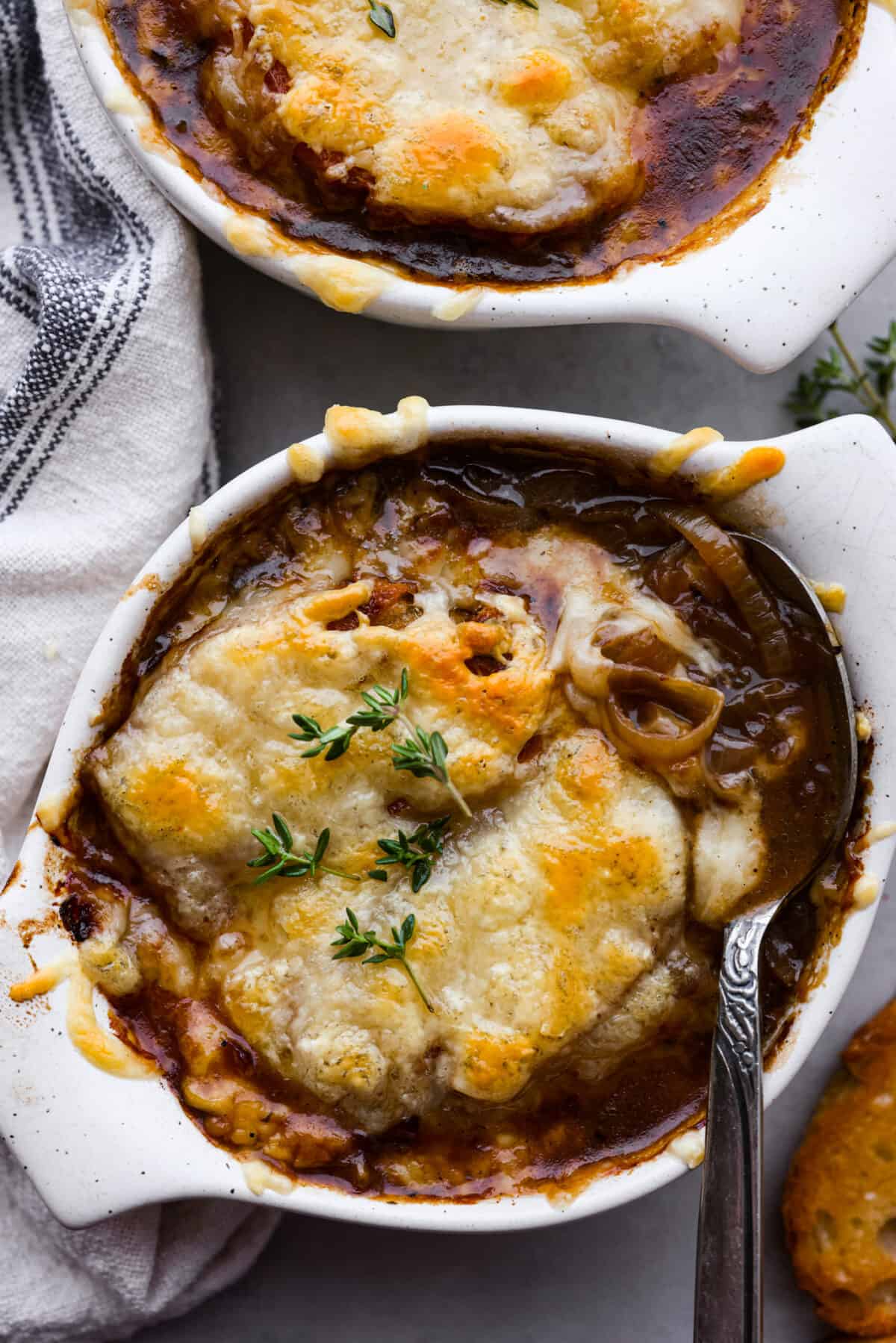French Onion Soup is such a classic and SO easy to make! Onions are slowly caramelized until soft and sweet, simmered with beef broth, thyme, sherry, and white wine. It's topped with a crispy crouton, loads of shredded gruyere cheese and broiled into a crispy, cheesy oblivion. So good! Top-down view of a bowl of French onion soup, topped with melted gruyere cheese.