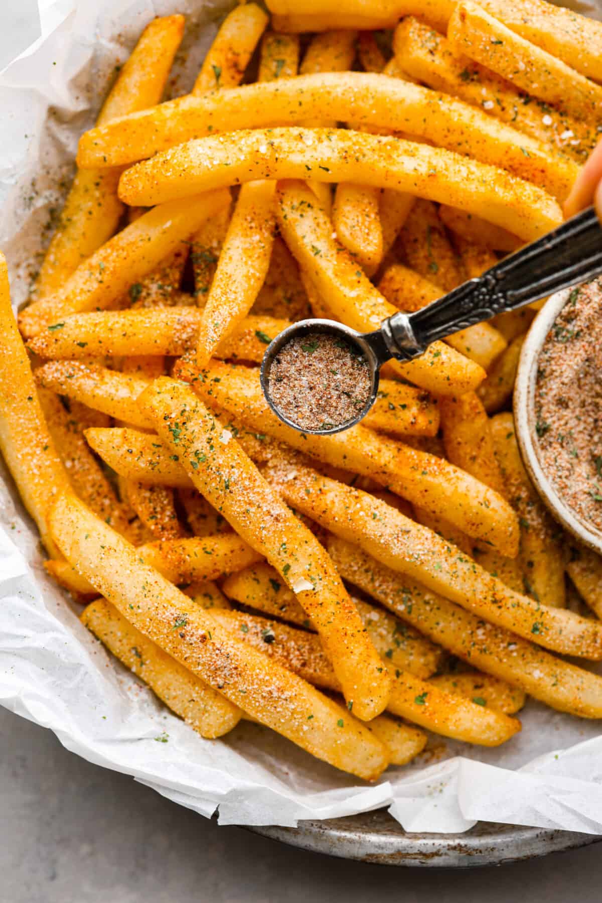Upgrade your fries with this perfected French fry seasoning! It's packed with flavor, making your homemade fries way better than the drive-thru ones. Fry seasoning being sprinkled on French fries.