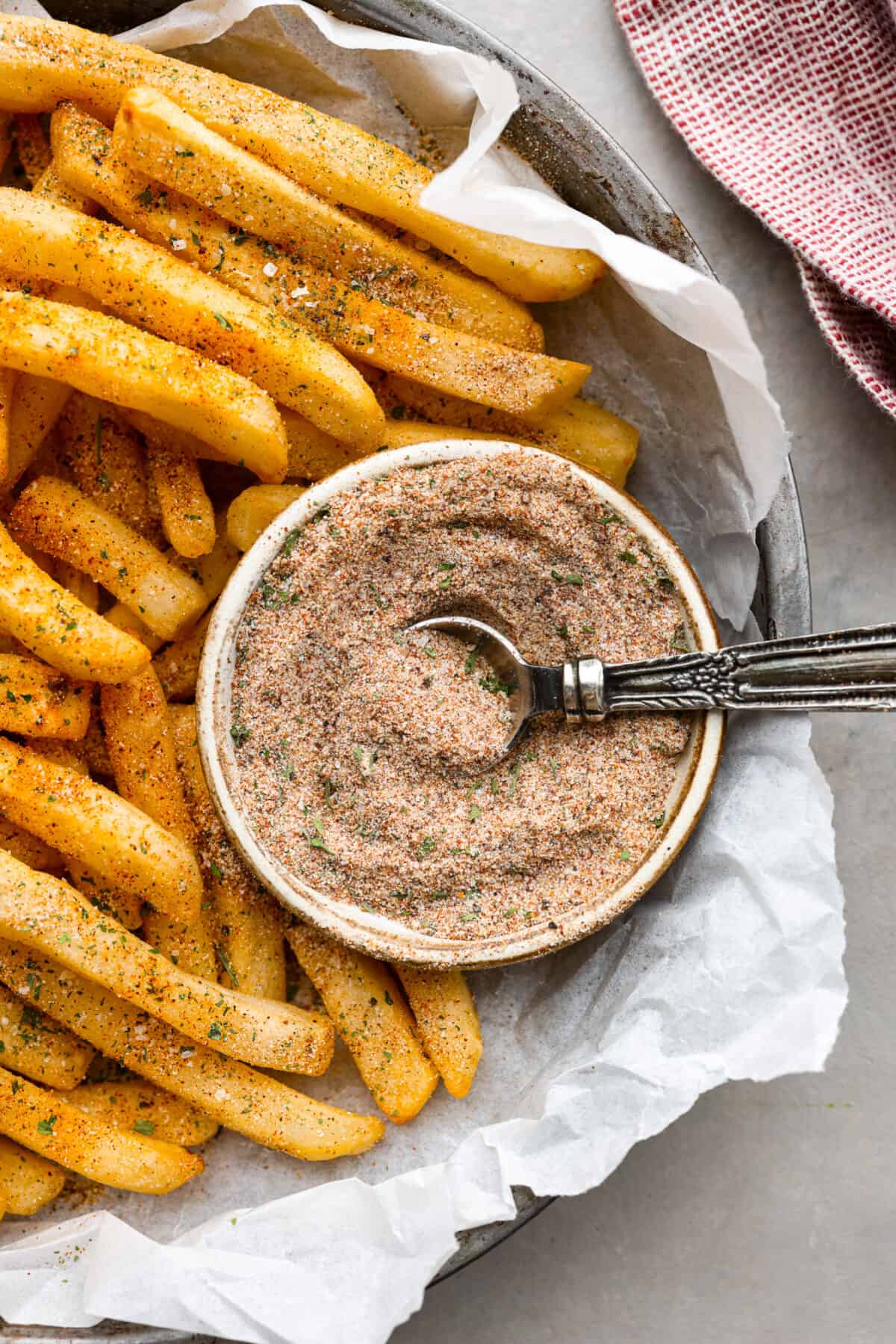 Upgrade your fries with this perfected French fry seasoning! It's packed with flavor, making your homemade fries way better than the drive-thru ones. A bowl of fry seasoning in a tin with some French fries next to it.
