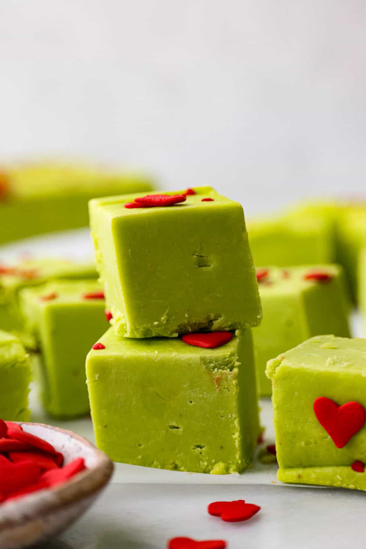 This delicious Grinch Fudge is easy to make and festive enough for any holiday gathering. Top it with red hearts, and voilร โ a yummy treat that might just make your heart grow bigger! A stack of grinch fudge.