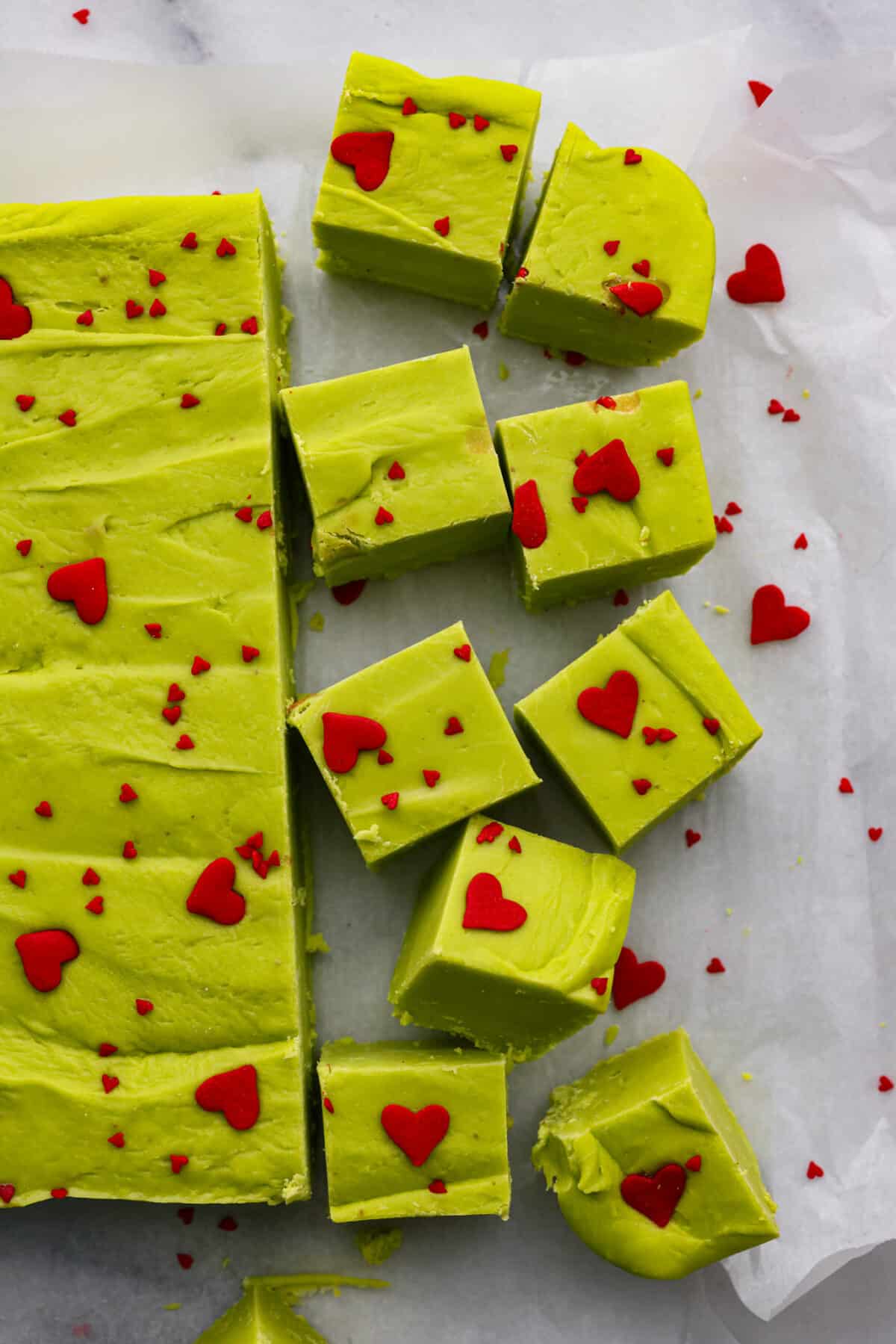 This delicious Grinch Fudge is easy to make and festive enough for any holiday gathering. Top it with red hearts, and voilร โ a yummy treat that might just make your heart grow bigger! The top view of Grinch fudge on parchment paper cut into cubes.