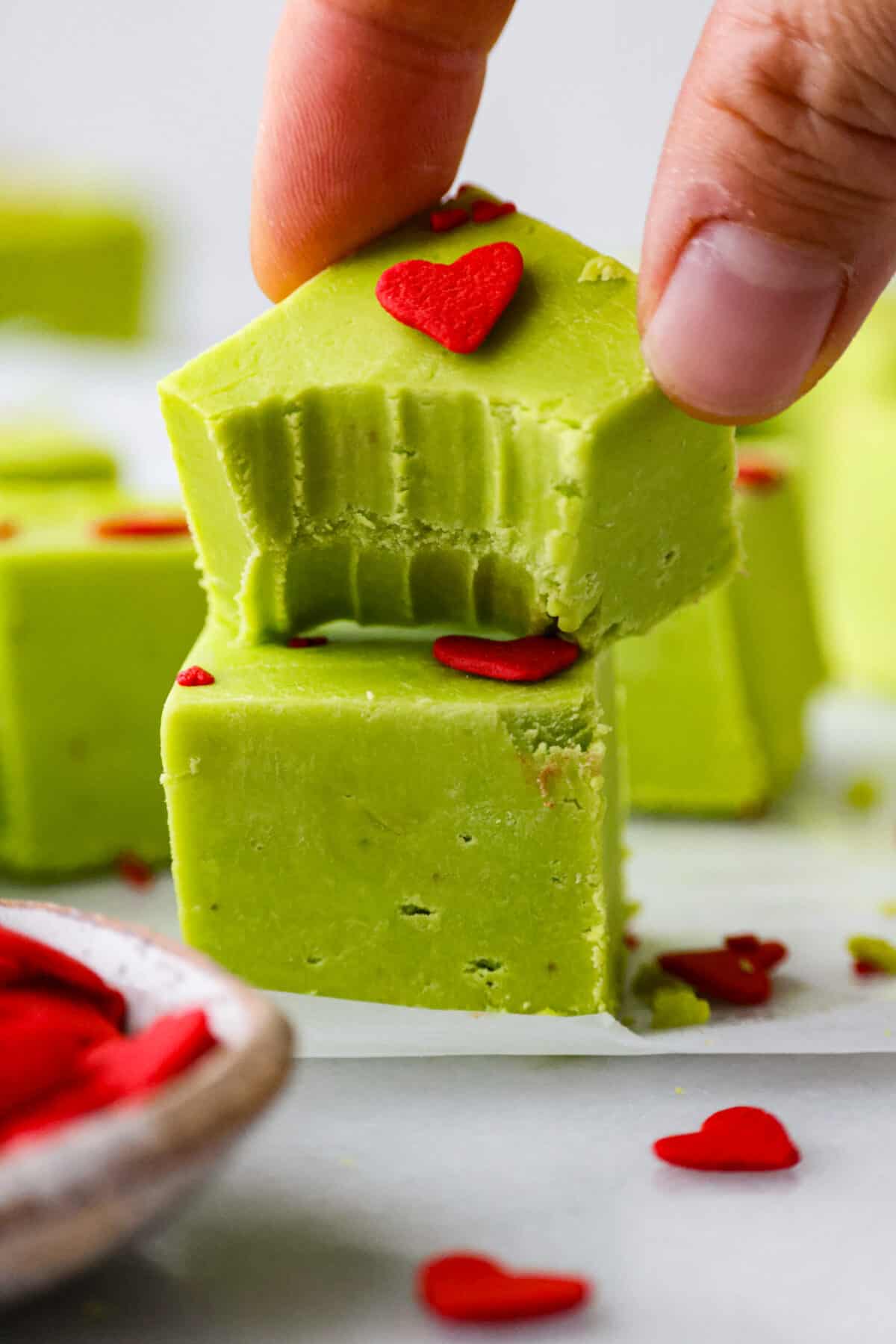 This delicious Grinch Fudge is easy to make and festive enough for any holiday gathering. Top it with red hearts, and voilร โ a yummy treat that might just make your heart grow bigger! A piece of Grinch fudge with a bite taken out of it.