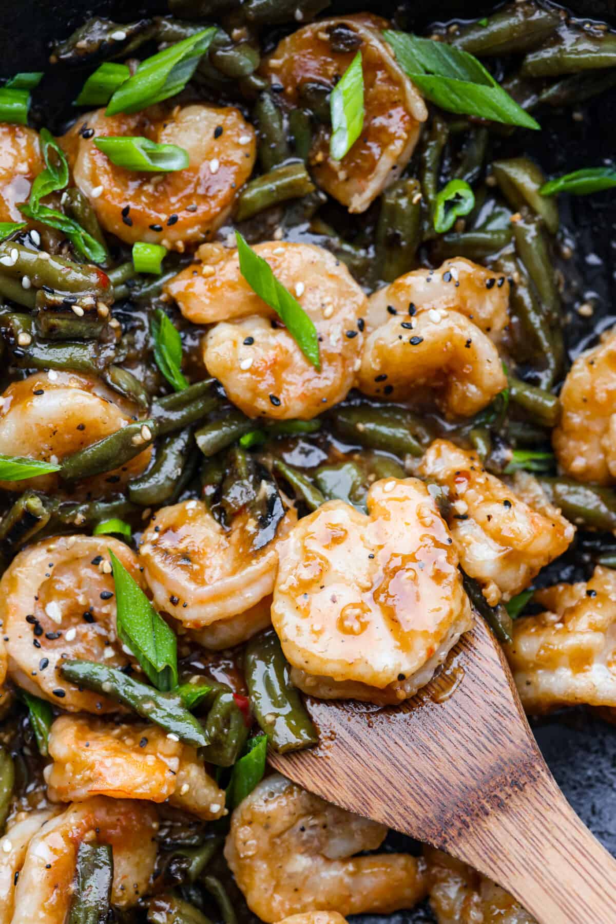 Crispy coated shrimp gets pan-fried to golden perfection in this better-than-takeout recipe! Tossed with tender veggies in a savory-sweet sauce, Hunan Shrimp is sure to be a new favorite in your dinner rotation. Closeup of Hunan shrimp being stirred with a wooden spoon.