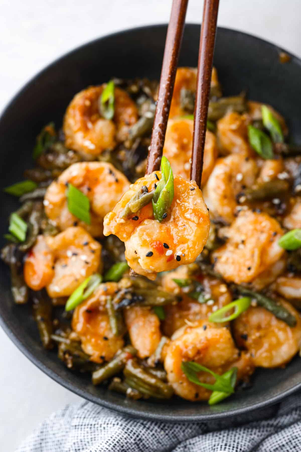 Crispy coated shrimp gets pan-fried to golden perfection in this better-than-takeout recipe! Tossed with tender veggies in a savory-sweet sauce, Hunan Shrimp is sure to be a new favorite in your dinner rotation. Picking up a piece of shrimp with chopsticks.