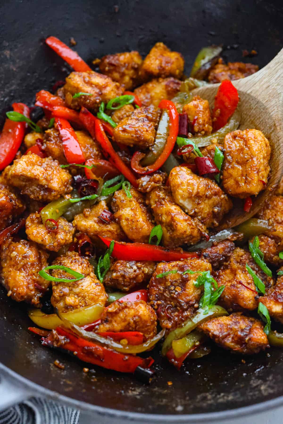 A takeout favorite for good reason! Kung pao chicken is pan-fried to crispy perfection and coated in a spicy, savory sauce that will leave you wanting more. Once you try making it from scratch, you won’t want it any other way! Closeup of kung pao chicken, being scooped up with a wooden spoon.