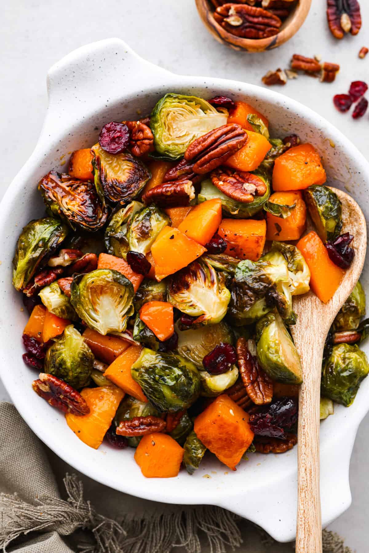 Simple to make and full of incredible flavor, maple roasted brussels sprouts and butternut squash is the perfect side dish. The veggies are crisp on the edges but soft and tender on the inside, tossed in a delicious maple glaze and surrounded by crunchy pecans and cranberries. Squash, brussels sprouts, and pecans served in a white baking dish.