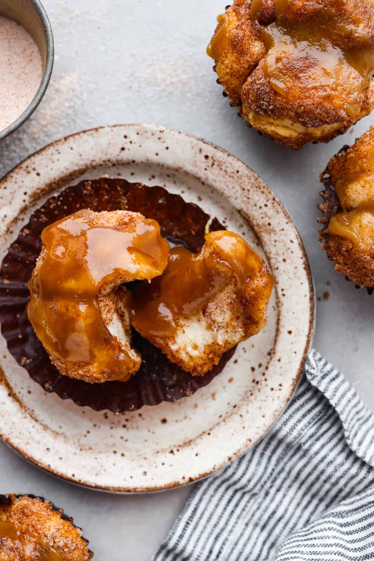 All the soft, ooey-gooey goodness of monkey bread in bite-sized form! Ready in less than 30 minutes, these monkey bread muffins are a quick and easy breakfast that everyone will love! A monkey bread muffin on a stoneware plate. It is torn in half.