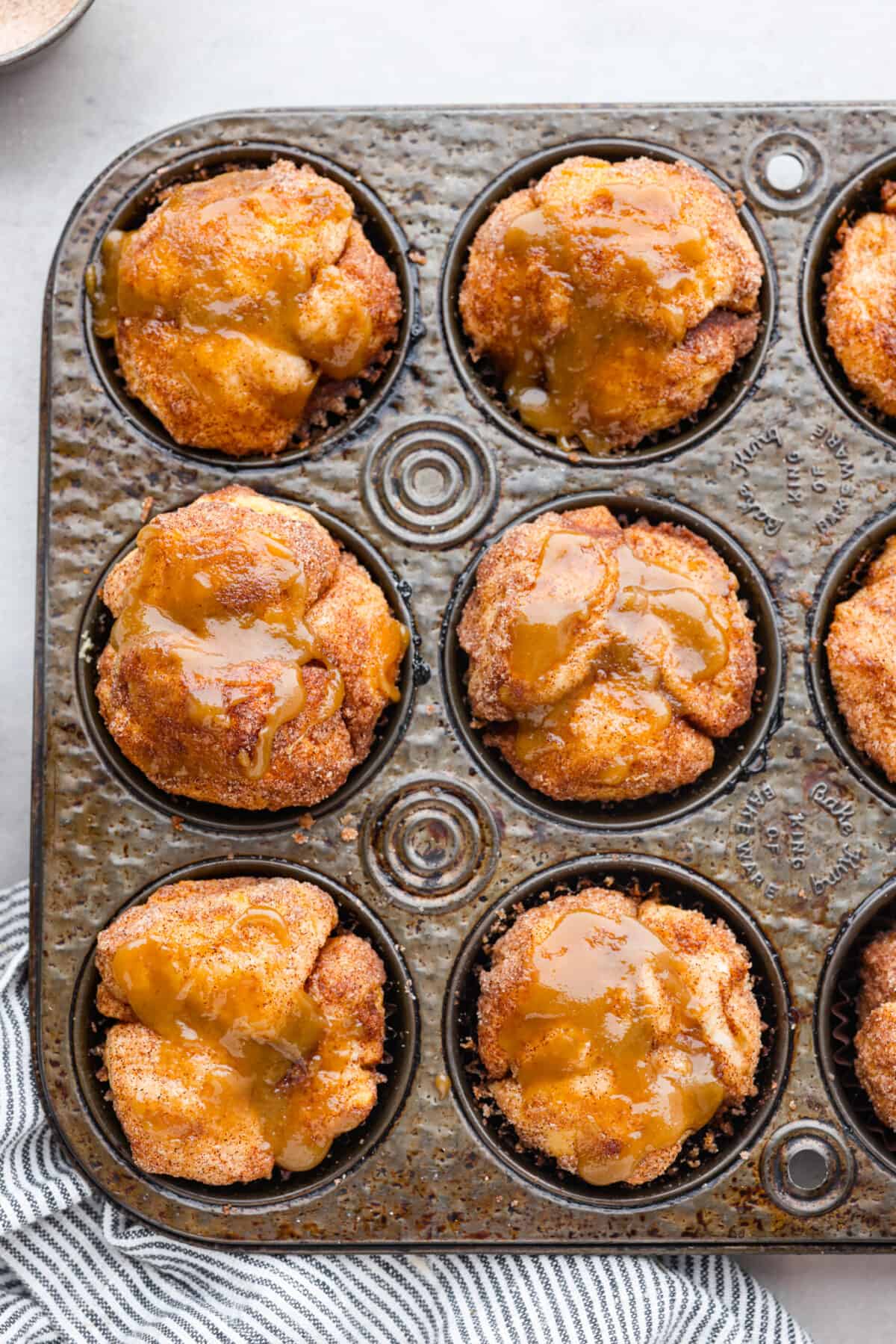 All the soft, ooey-gooey goodness of monkey bread in bite-sized form! Ready in less than 30 minutes, these monkey bread muffins are a quick and easy breakfast that everyone will love! Top-down view of monkey bread muffins in a muffin tin.