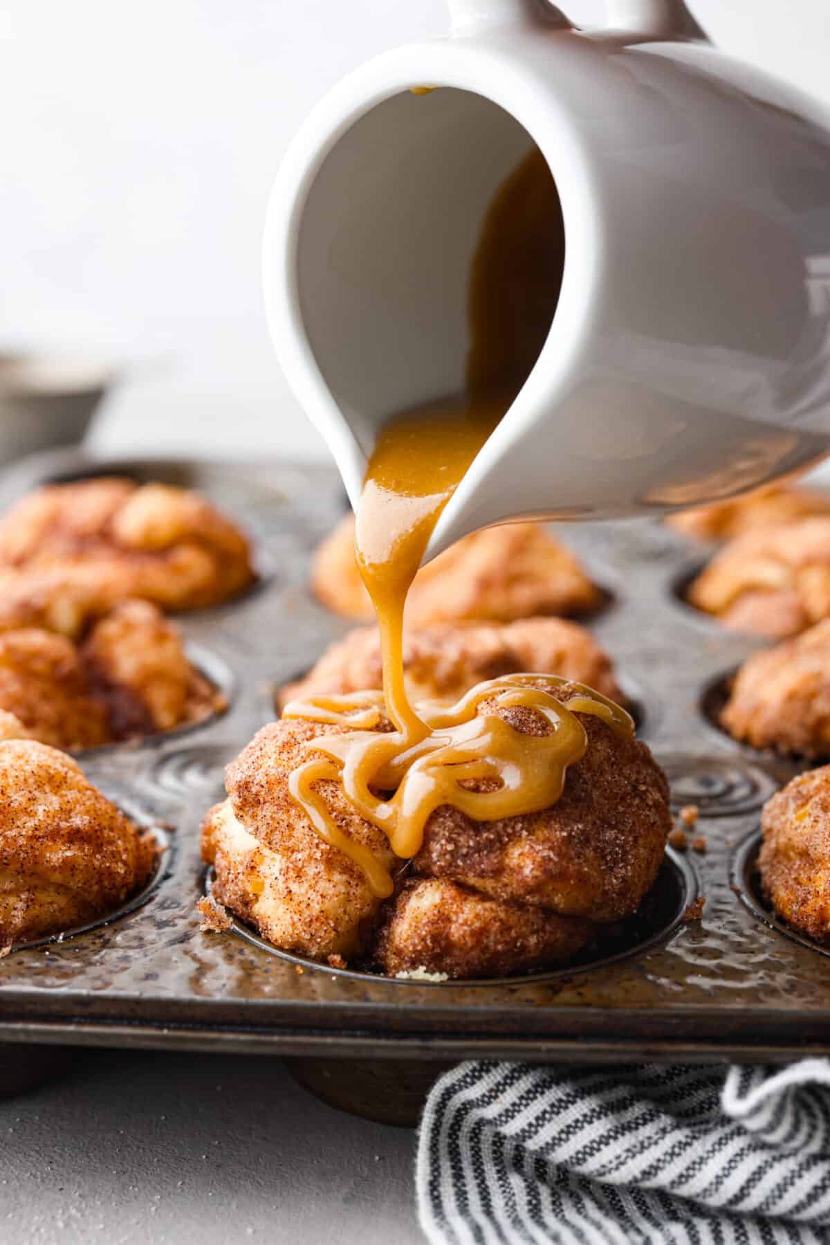 All the soft, ooey-gooey goodness of monkey bread in bite-sized form! Ready in less than 30 minutes, these monkey bread muffins are a quick and easy breakfast that everyone will love! Pouring caramel sauce over a muffin.