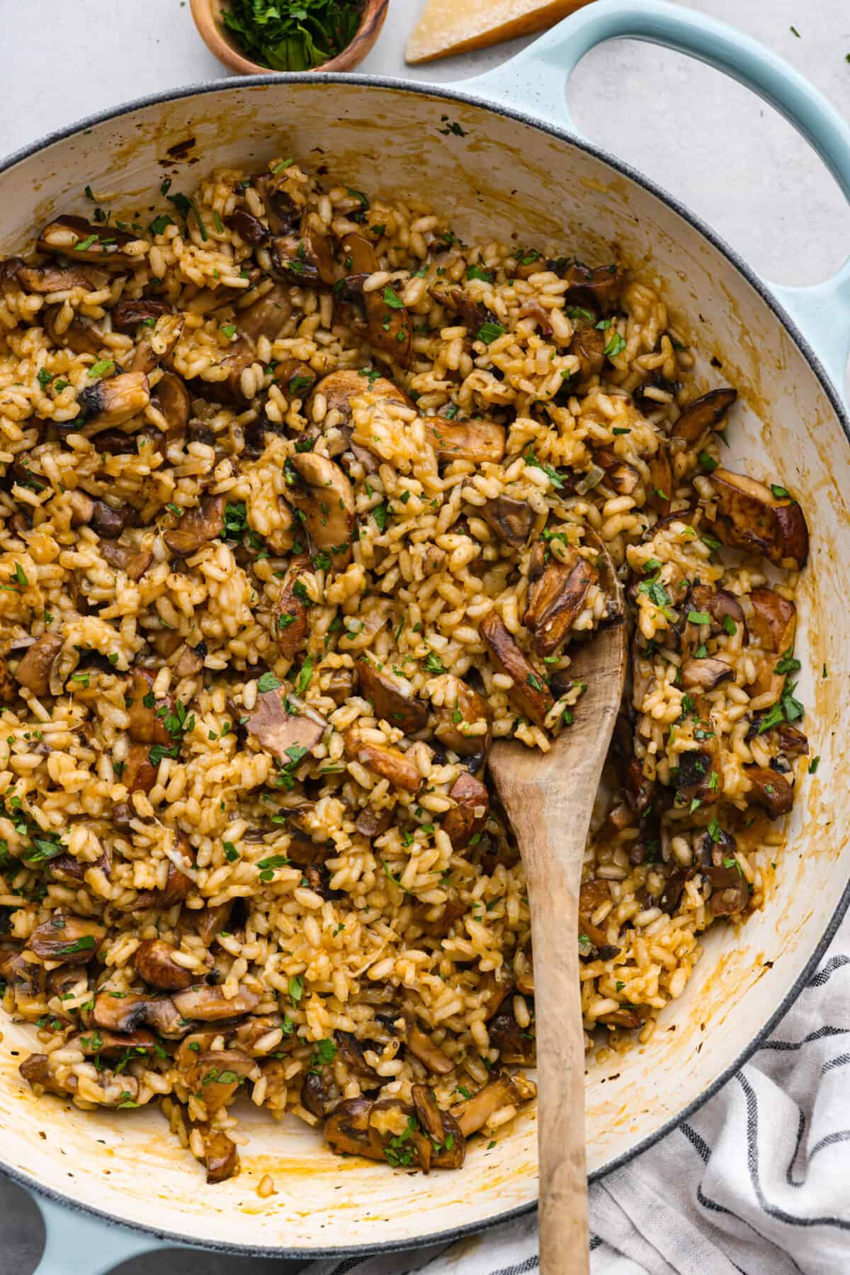 A creamy, hearty side dish that you'll want to serve with everything. Mushroom risotto is made with tender sauteed mushrooms and arborio rice simmered to perfection in a garlic, shallot, and white wine sauce. Top it off with some shredded parmesan for a tasty dish that will rival the main course! Top-down view of mushroom risotto in a blue and white skillet.