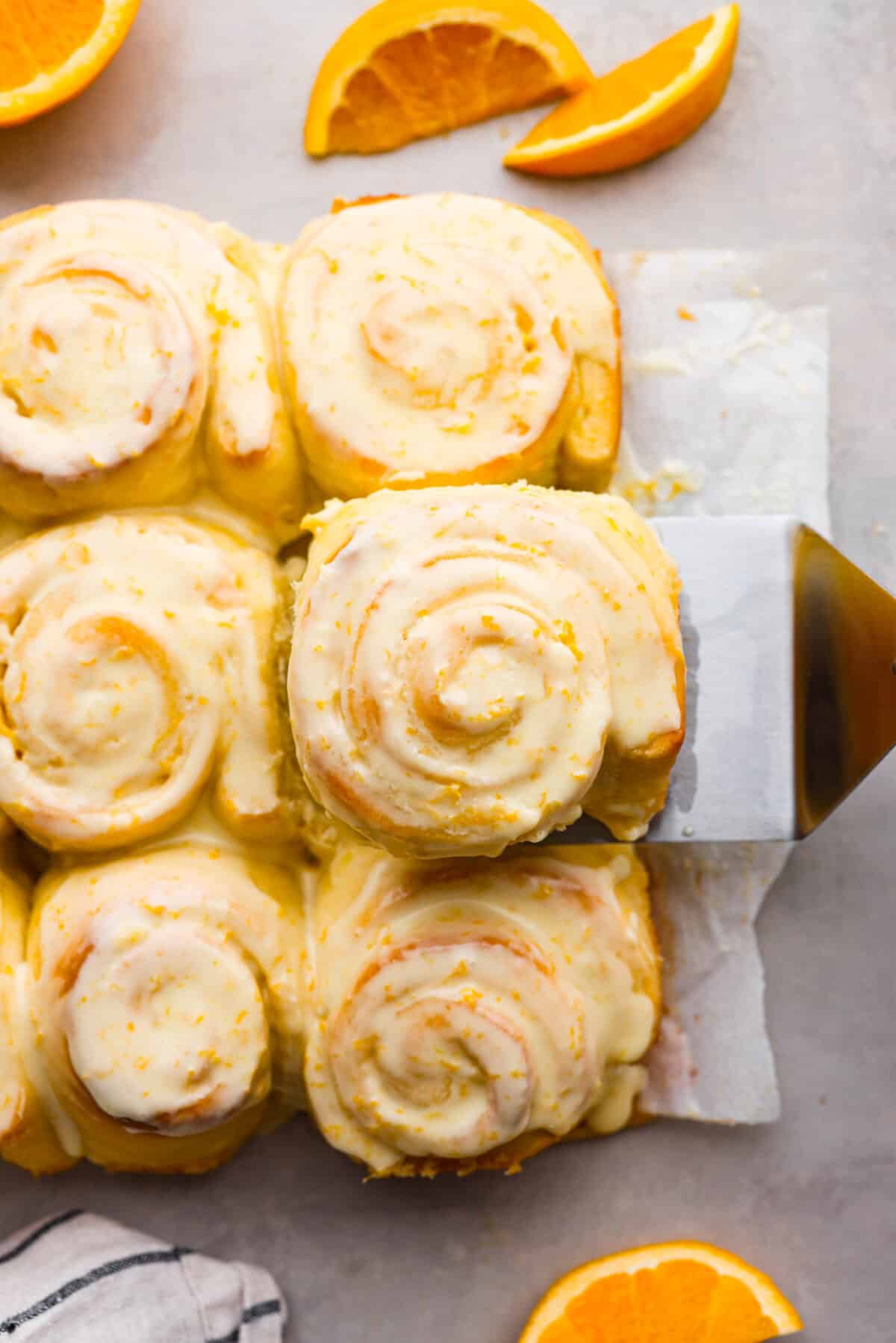 Sticky and soft with a vibrant orange flavor, these orange rolls are the best youโll find. Simple to make, these are the zesty sister to a cinnamon roll! The top view of orange rolls on parchment paper surrounded by orange slices.