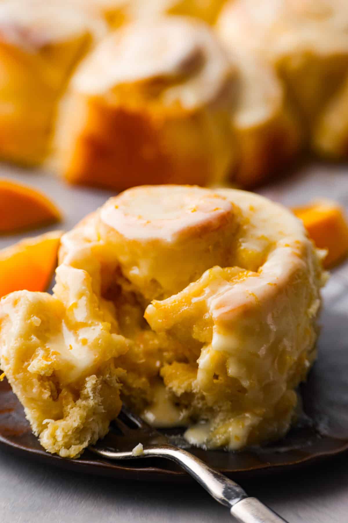 Sticky and soft with a vibrant orange flavor, these orange rolls are the best youโll find. Simple to make, these are the zesty sister to a cinnamon roll! A close up of an orange roll on a plate with a fork.