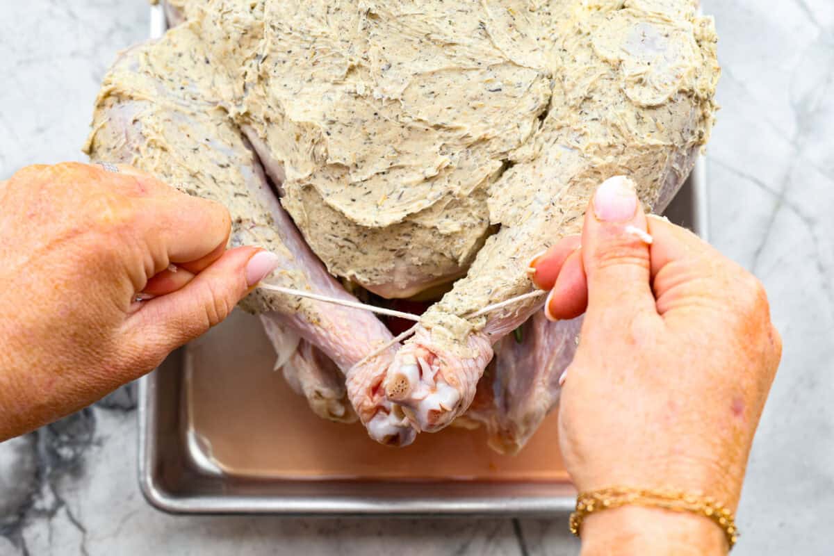 Look no further! This roasted turkey recipe is the absolute juiciest, fool-proof turkey recipe you will ever need. You'll have the confidence to make a perfect turkey every time. This deliciously seasoned turkey will be the star of your Thanksgiving meal! Ninth photo of the legs being tied with twine.