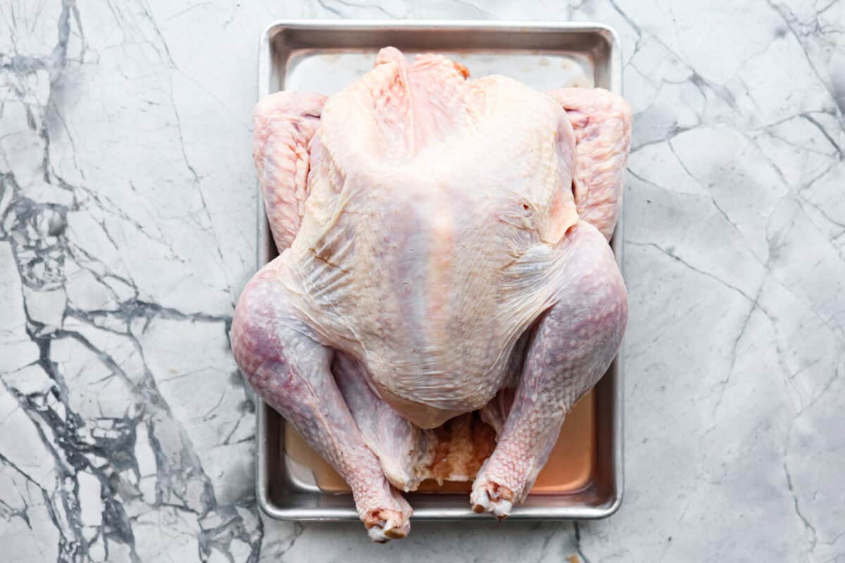 Look no further! This roasted turkey recipe is the absolute juiciest, fool-proof turkey recipe you will ever need. You'll have the confidence to make a perfect turkey every time. This deliciously seasoned turkey will be the star of your Thanksgiving meal! First photo of the turkey on a sheet pan.