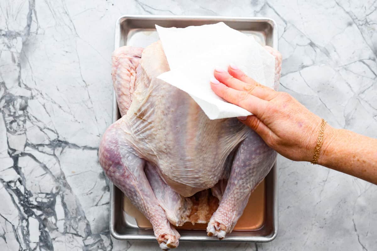 Look no further! This roasted turkey recipe is the absolute juiciest, fool-proof turkey recipe you will ever need. You'll have the confidence to make a perfect turkey every time. This deliciously seasoned turkey will be the star of your Thanksgiving meal! Third photo of a paper towel patting the turkey dry.