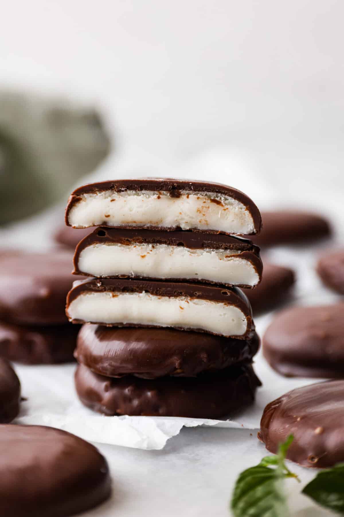 These homemade peppermint patties are miles ahead of anything you'll find at the store, and making them is a breeze. They're soft and pillowy, packed with mint chocolate flavor that will leave you wanting more! 5 peppermint patties stacked on top of each other, a few of them are broken in half so the filling can be seen.