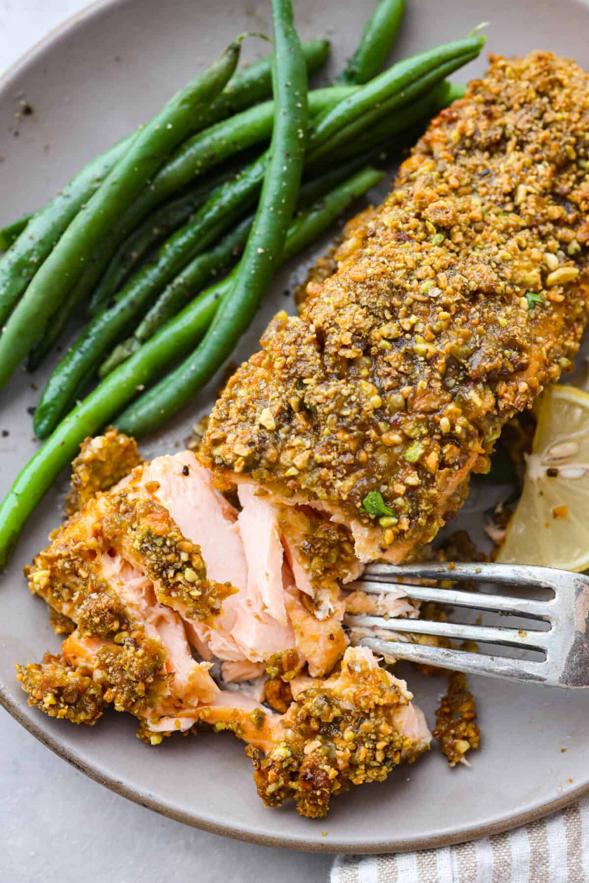 Delicious Pistachio Crusted Salmon is a savory entree that is coated in a mix of garlic, Dijon mustard, honey, and lemon juice with a crunchy pistachio crust all baked to perfection. Ready in just 30 minutes! Closeup of a salmon filet with a bite taken out of it.