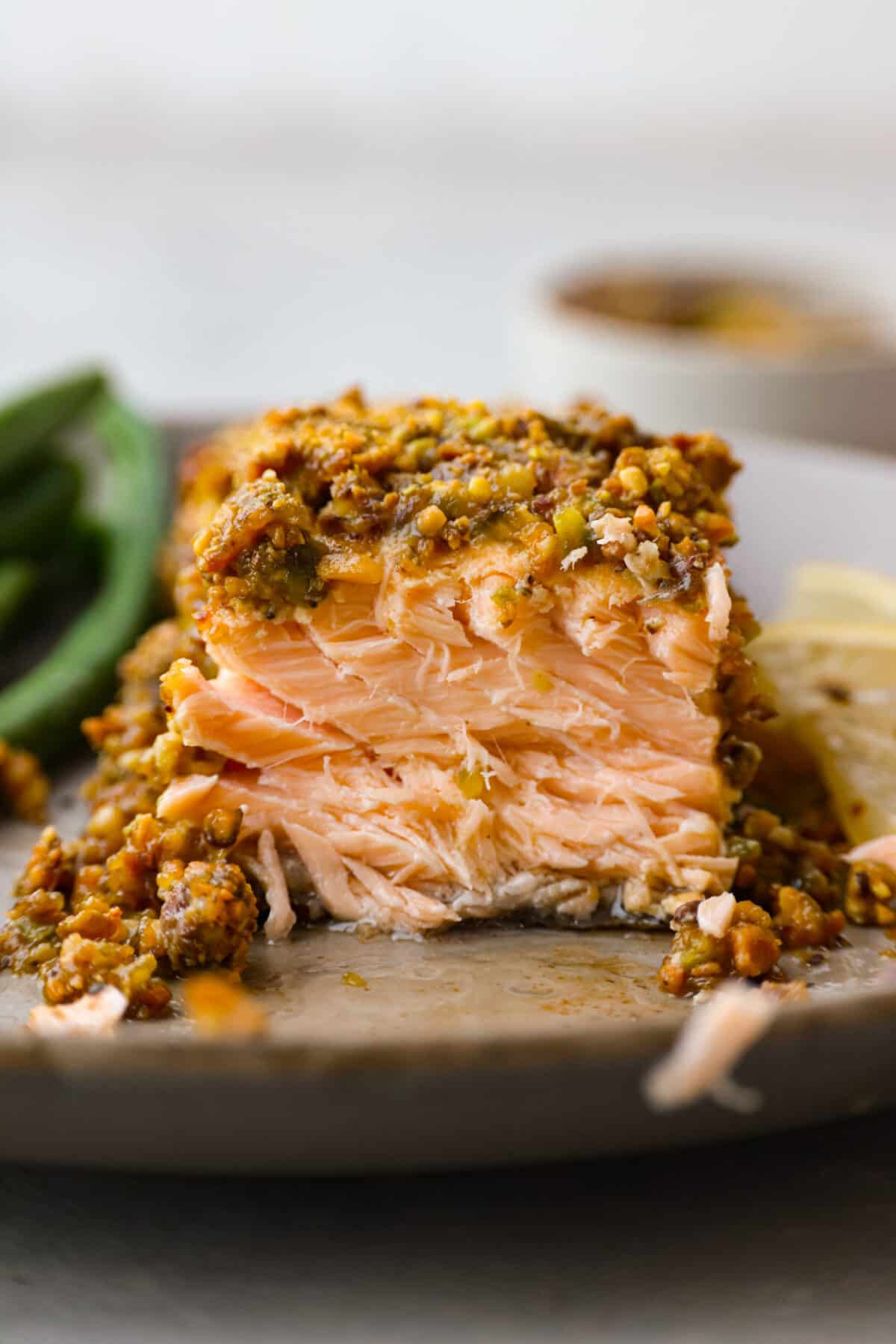 Delicious Pistachio Crusted Salmon is a savory entree that is coated in a mix of garlic, Dijon mustard, honey, and lemon juice with a crunchy pistachio crust all baked to perfection. Ready in just 30 minutes! Front view of a salmon filet with a bite taken out of it.