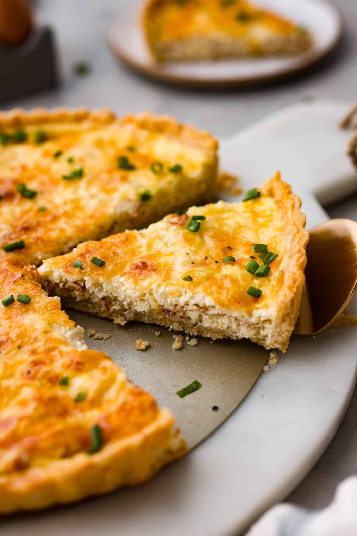 Flavorfulย Quiche Lorraineย is a classic French breakfast recipe. Itโs a simple, yet incredible combination of bacon, shallots, creamy egg custard and cheese, all baked in a flaky pie crust. Perfect for breakfast, brunch, or any meal of the day! A slice of quiche being served with a metal spatula.