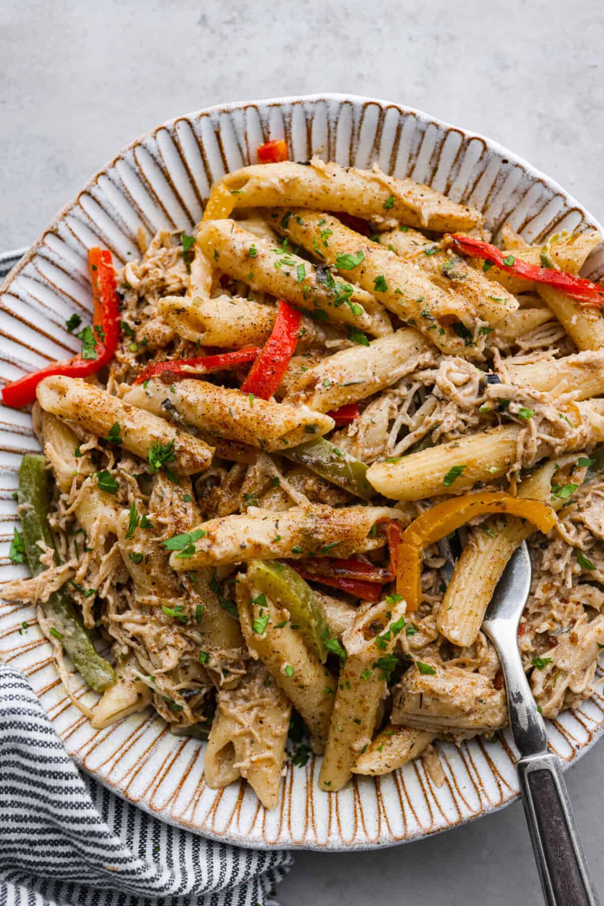 This incredibly flavorful Rasta Pasta recipe features penne pasta cooked al dente and tossed with sautรฉed peppers and shredded chicken in a rich, creamy, spiced sauce. Rasta pasta served in a white scalloped stoneware bowl.