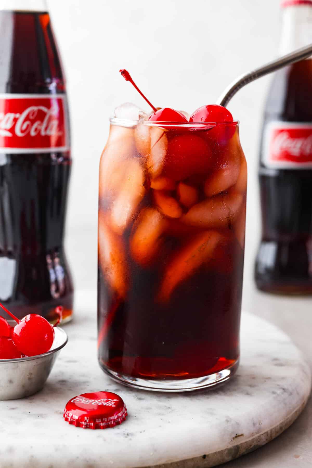 The whole family will love this fun Roy Rogers drink made with Coca-Cola, grenadine syrup, and Maraschino cherries on top! Only 3 simple ingredients to enjoy this classic non-alcoholic drink. Close view of Roy Rogers drink in a tall glass with ice and cherries on top.