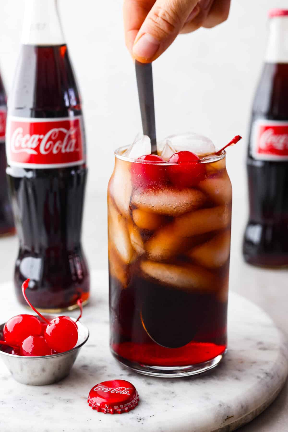The whole family will love this fun Roy Rogers drink made with Coca-Cola, grenadine syrup, and Maraschino cherries on top! Only 3 simple ingredients to enjoy this classic non-alcoholic drink. Close view of a spoon stirring the Roy Rogers drink.