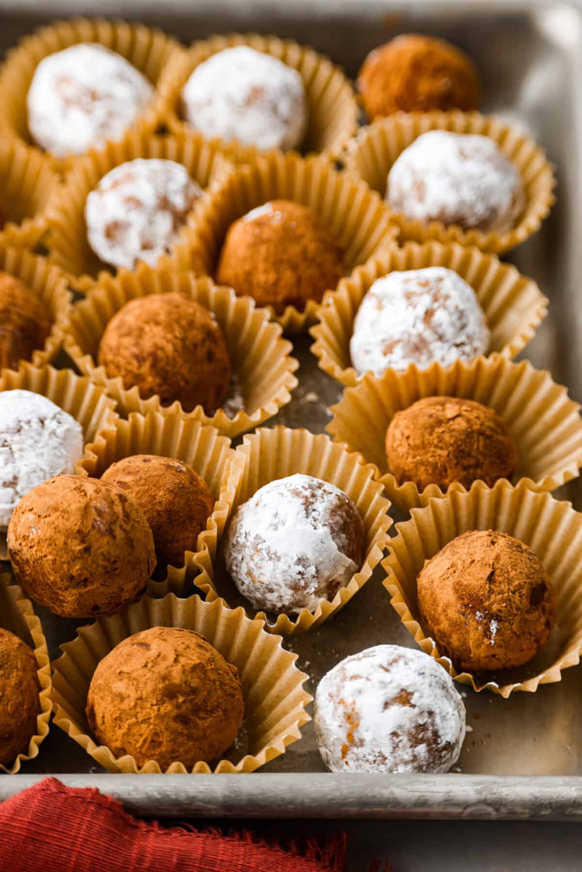 Easy and impressive rum balls are perfect for the holidays! Vanilla wafer crumbs, powdered sugar, cocoa powder, and rum create a truffle-like consistency bursting with rich flavors. A simple bite-sized dessert that every party needs! Close side view of rum balls in mini muffin cups.