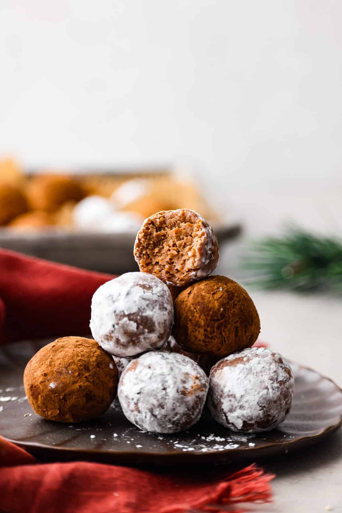 Easy and impressive rum balls are perfect for the holidays! Vanilla wafer crumbs, powdered sugar, cocoa powder, and rum create a truffle-like consistency bursting with rich flavors. A simple bite-sized dessert that every party needs! Close view of rum balls stacked on a brown plate.