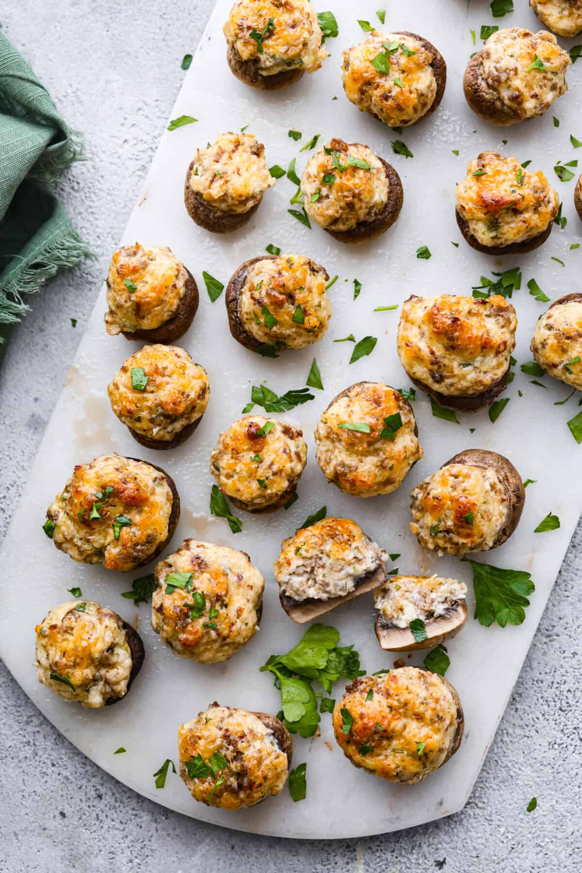 Sausage Stuffed Mushrooms are stuffed mushroom caps filled with a creamy and delicious mixture of onions, garlic, chopped mushroom stems, and sausage! These are a must-make for your next party! Top-down view of sausage stuffed mushrooms on a serving platter.