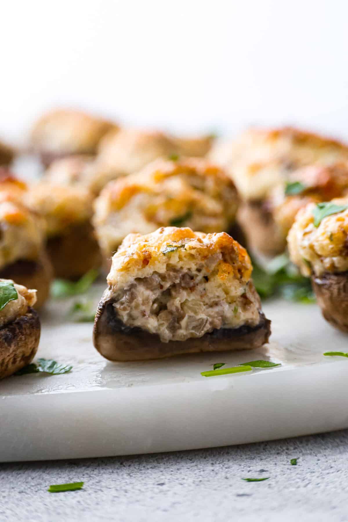Sausage Stuffed Mushrooms are stuffed mushroom caps filled with a creamy and delicious mixture of onions, garlic, chopped mushroom stems, and sausage! These are a must-make for your next party! A sausage stuffed mushroom cut in half.