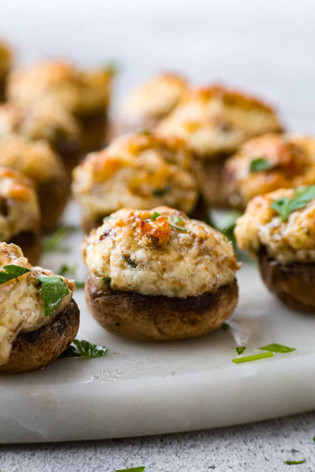 Sausage Stuffed Mushrooms are stuffed mushroom caps filled with a creamy and delicious mixture of onions, garlic, chopped mushroom stems, and sausage! These are a must-make for your next party! Closeup of a button mushroom filled with a cream cheese and sausage mixture.