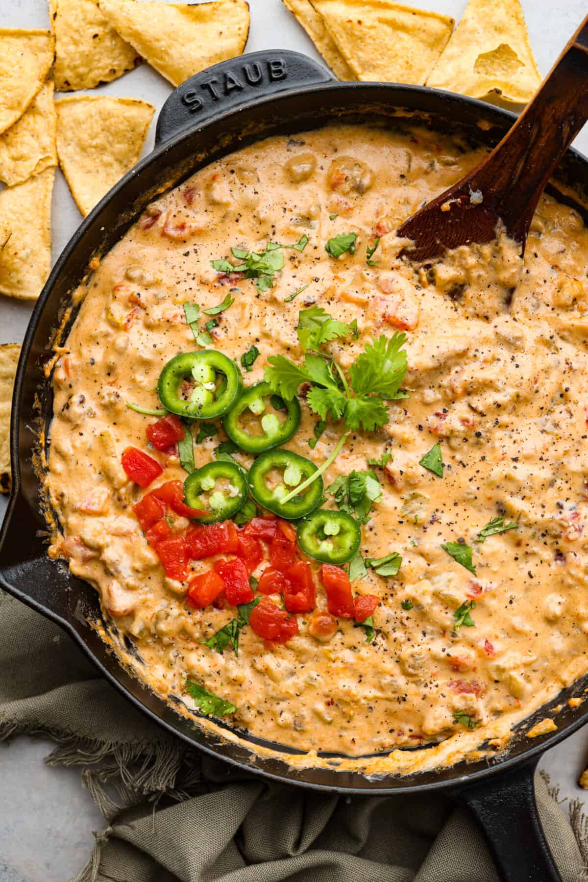 Sausage dip is a must-make appetizer for any potluck, party, or get-together! Crumbled sausage, cream cheese, pepper jack, chopped tomatoes and green chiles get cooked together to melty perfection. Sausage dip in a black skillet, garnished with chopped jalapenos.