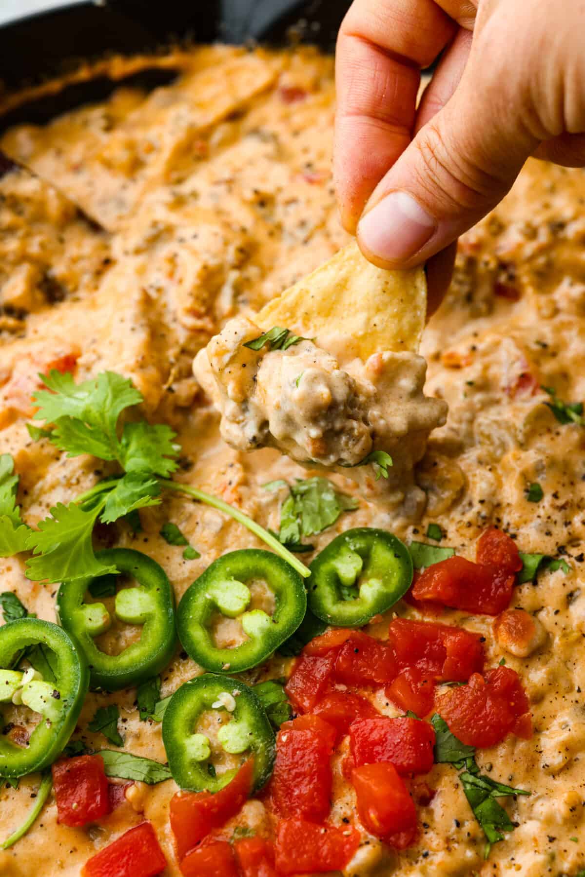 Sausage dip is a must-make appetizer for any potluck, party, or get-together! Crumbled sausage, cream cheese, pepper jack, chopped tomatoes and green chiles get cooked together to melty perfection. Dipping a tortilla chip into the cheesy dip.