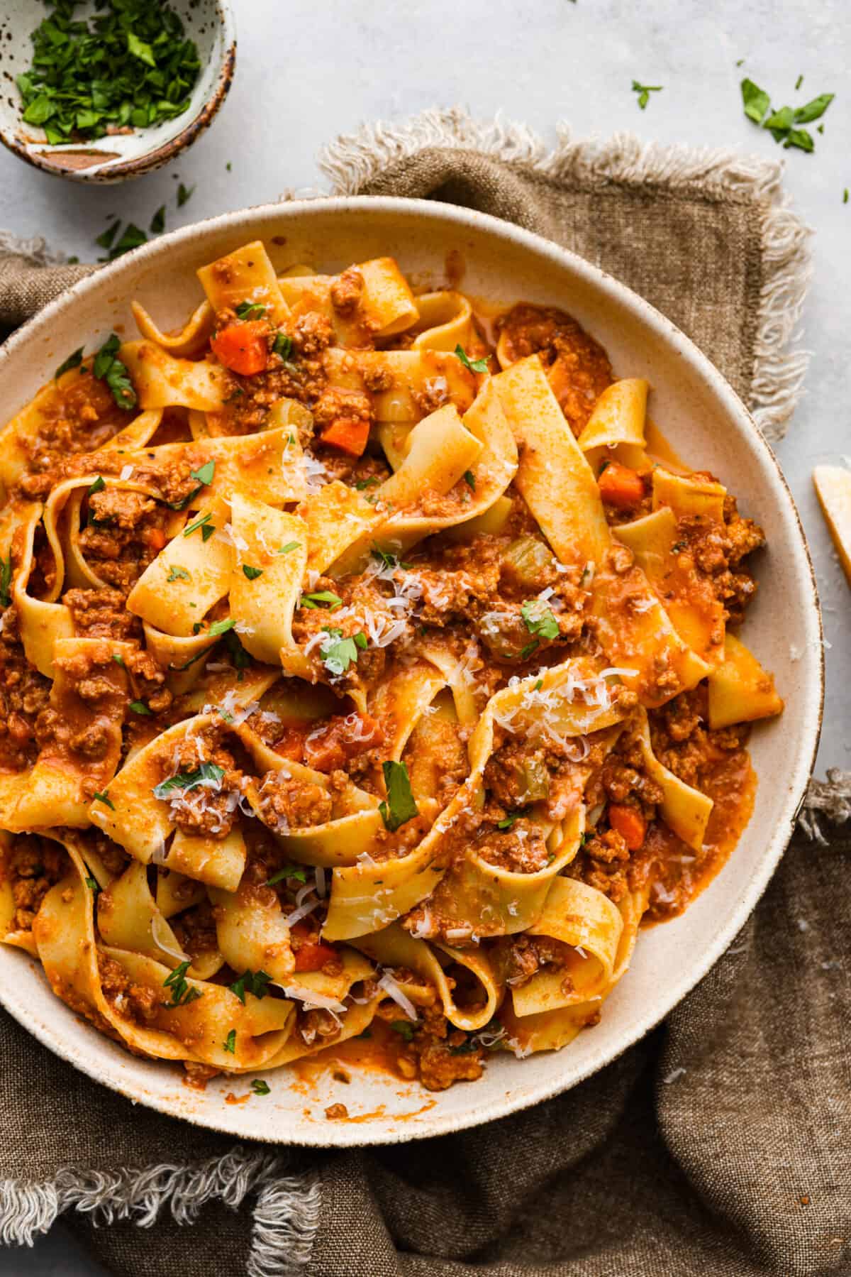 This Slow Cooker Ragu recipe is an easy-to-make comfort food that your whole family will love! Not to mention it makes a LOT and is freezer-friendly! A bowl of ragu with pasta. Topped with fresh parsley and freshly grated cheese.