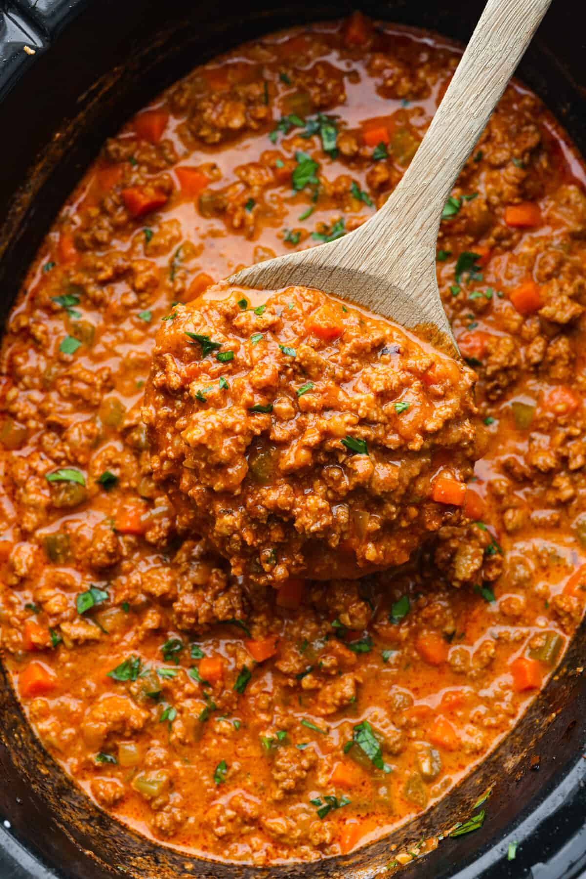 This Slow Cooker Ragu recipe is an easy-to-make comfort food that your whole family will love! Not to mention it makes a LOT and is freezer-friendly! Finished ragu sauce in the slow cooker with a wooden spoon scooping some out.