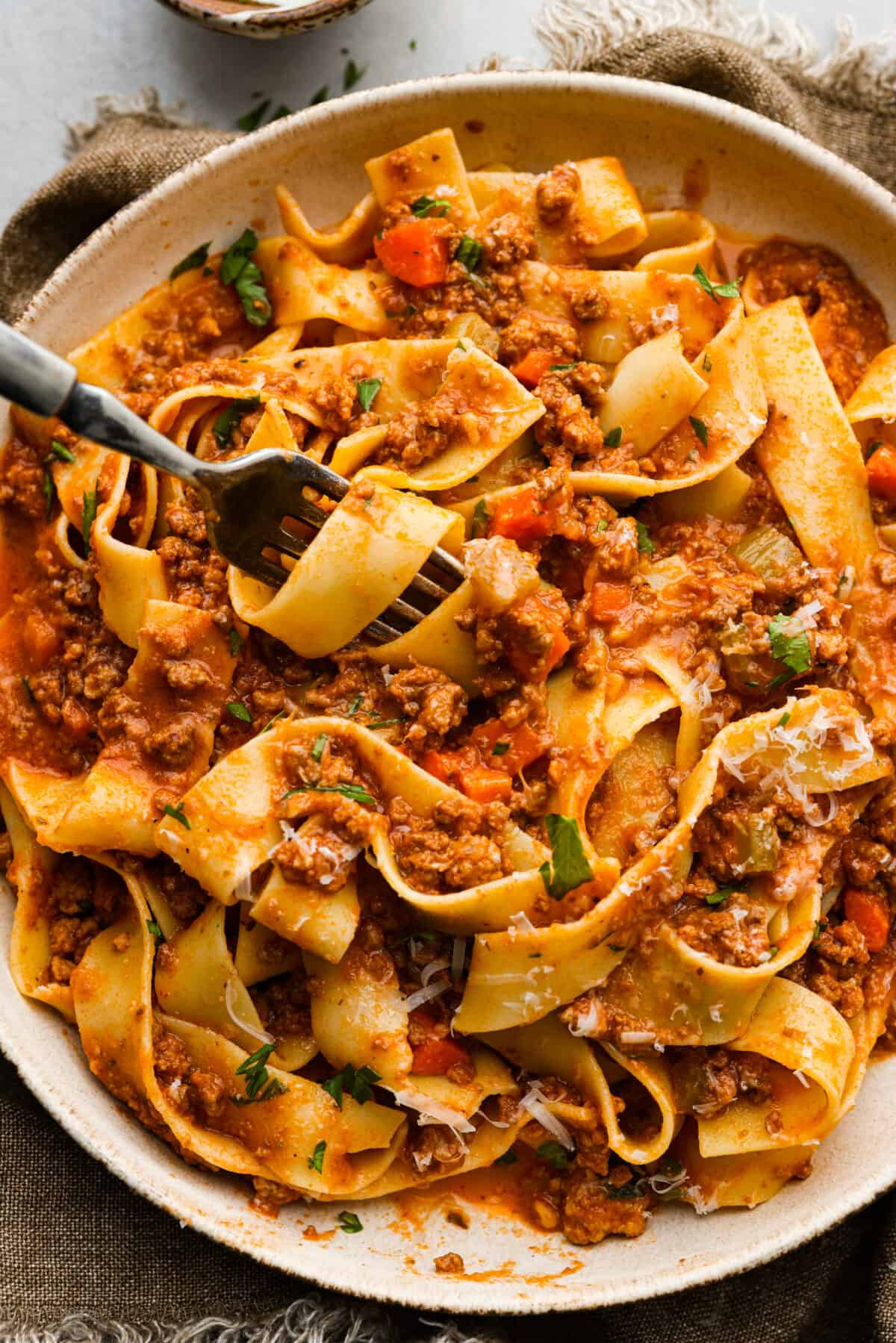 This Slow Cooker Ragu recipe is an easy-to-make comfort food that your whole family will love! Not to mention it makes a LOT and is freezer-friendly! A closeup of slow cooker ragu with pasta in a bowl with a fork that has some pasta swirled around it.