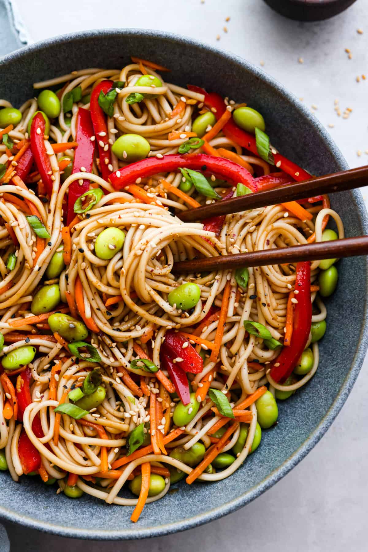 This vibrant soba noodle salad bursts with flavor and color, thanks to its medley of crunchy veggies, nutty sesame seeds, and a zingy ginger-lime dressing. It's light and refreshing, perfect for a quick lunch or a satisfying side dish! Closeup of soba pasta salad and brown chopsticks.