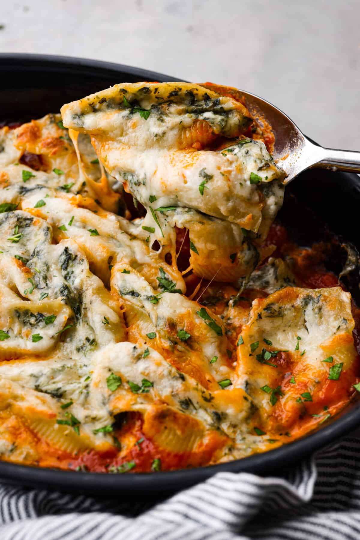 This recipe for spinach stuffed shells features tender, jumbo pasta shells filled to the brim with a tasty mixture of garlic, parmesan, ricotta cheese, chopped spinach, and Italian seasonings. Covered with a layer of bubbly marinara sauce, this is the most delicious way to load up on carbs! Closeup of spinach stuffed shells being scooped up with a large metal spoon.