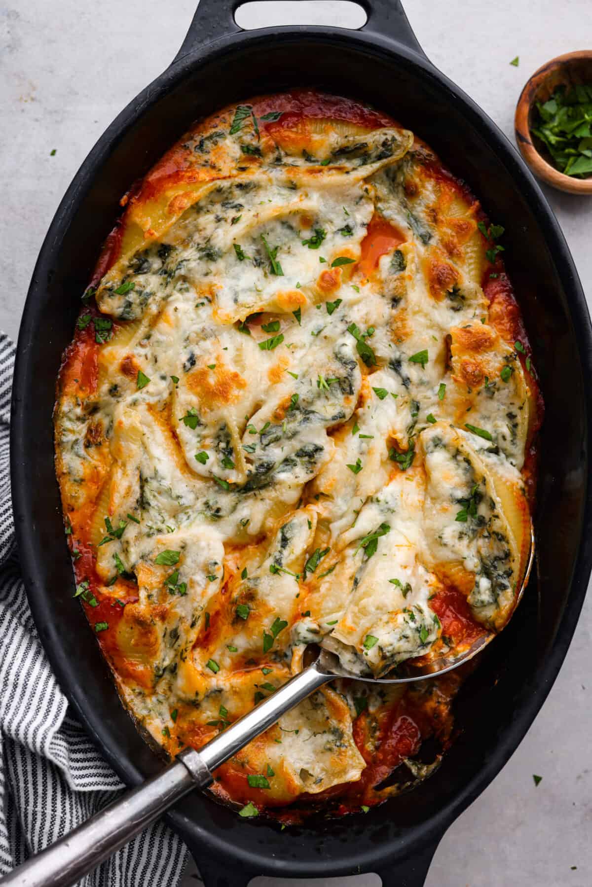 This recipe for spinach stuffed shells features tender, jumbo pasta shells filled to the brim with a tasty mixture of garlic, parmesan, ricotta cheese, chopped spinach, and Italian seasonings. Covered with a layer of bubbly marinara sauce, this is the most delicious way to load up on carbs! Top-down view of baked, stuffed shells in a black casserole dish.