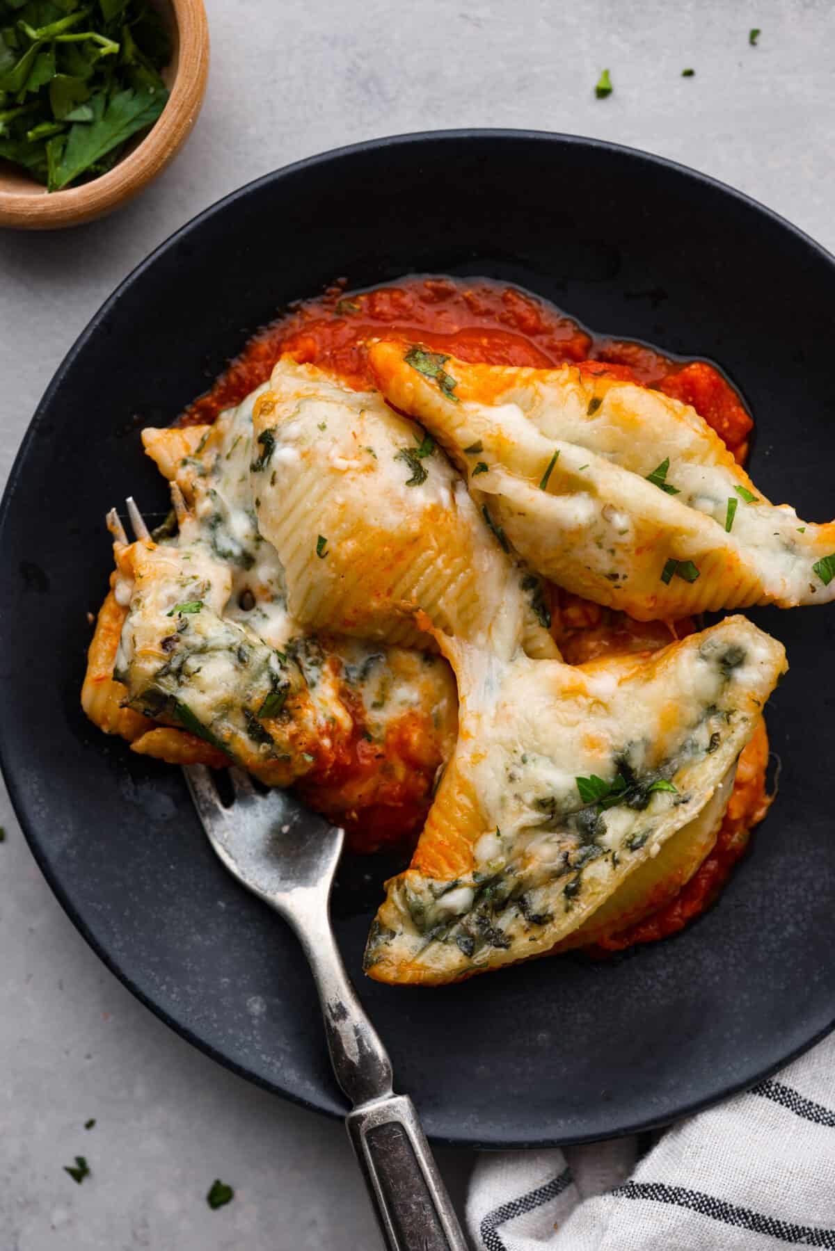 This recipe for spinach stuffed shells features tender, jumbo pasta shells filled to the brim with a tasty mixture of garlic, parmesan, ricotta cheese, chopped spinach, and Italian seasonings. Covered with a layer of bubbly marinara sauce, this is the most delicious way to load up on carbs! A serving of pasta on a black plate.