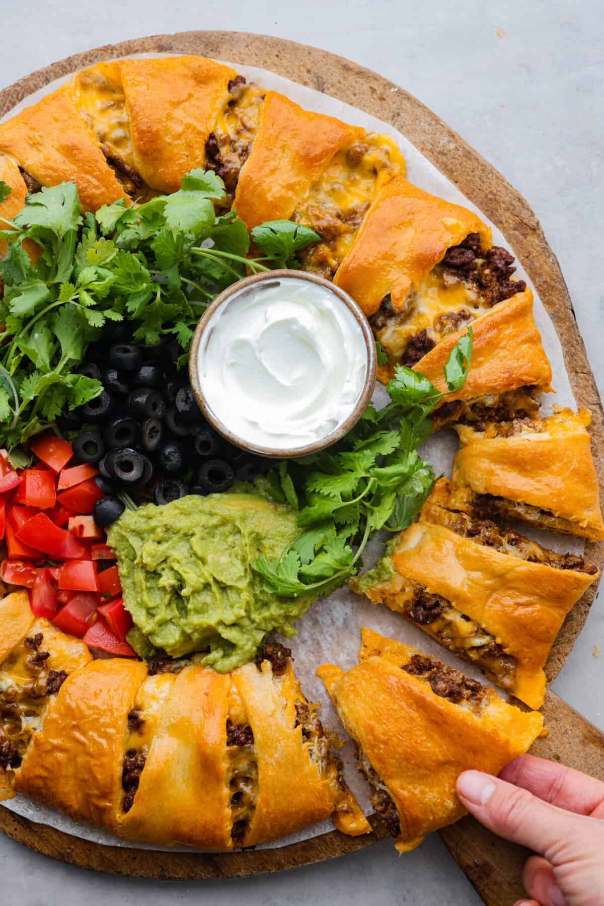 This taco ring is the easiest, cheesiest dinner. I know your family will love it as much as mine does! All you need is a can of crescent rolls, shredded Colby Jack cheese, some taco seasoning, and your favorite fixings to bring it to life! Picking up a piece of the taco ring.