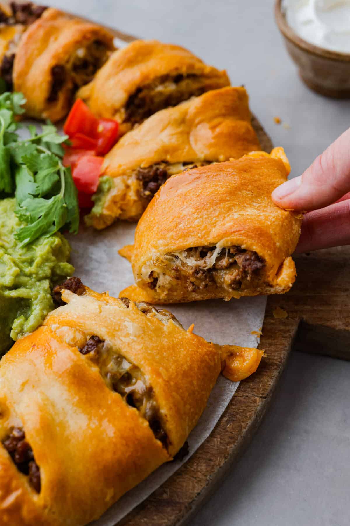 This taco ring is the easiest, cheesiest dinner. I know your family will love it as much as mine does! All you need is a can of crescent rolls, shredded Colby Jack cheese, some taco seasoning, and your favorite fixings to bring it to life! Closeup of crescent roll dough filled with melted colby jack cheese and ground beef.